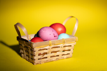 Homemade colored Easter eggs in small wooden basket on the yellow background  ready for Easter