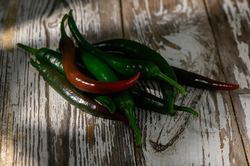 Assortment of vibrant green and red chilies resting on rustic wooden surface under soft light
