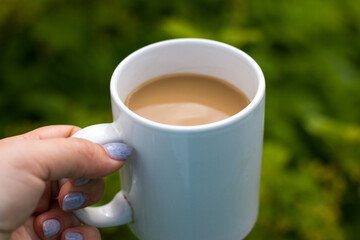A woman's hand holds a mug with a hot drink against the background of nature