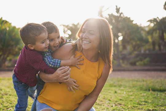 Happy young mother having playful time with twin son children at city park during sunset time - Mother's day, family love and single parent concept