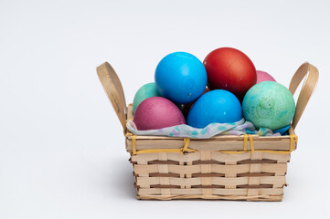 Colored Easter eggs in small wooden basket isolated on the white background.