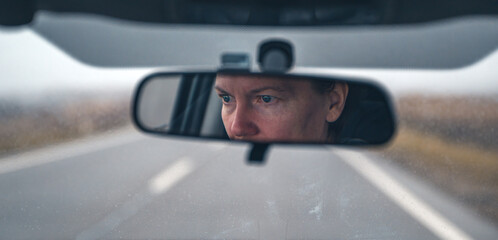 Female driver face at car rear view mirror on a rainy day - obrazy, fototapety, plakaty