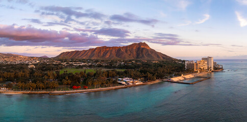 Fototapeta premium Aerial view of Diamond Head Crater on Oahu Island, Hawaii, at sunset. Turquoise waters, palm lined shore, and high rise buildings are visible.