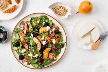 Spinach salad with crispy bacon, pear, cheese, chopped walnuts and blackberries on white background