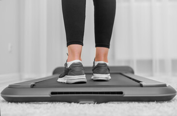 A person wearing black leggings and gray sneakers is walking on a compact treadmill in a modern, minimalistic home environment, focusing on fitness and an active lifestyle.