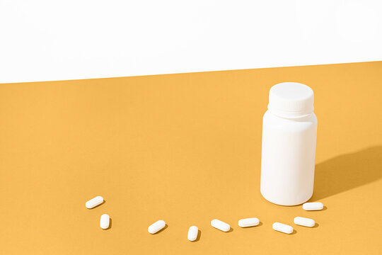 White pill bottle and pills on a vibrant yellow background
