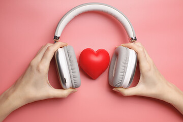 hands holding headphones embrace red heart on a soft pink background, symbolizing favorite music. A perfect concept for audio passion, romance, and playlist themes.