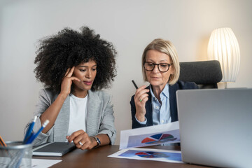 Two beautiful female colleagues interacting while working in office.