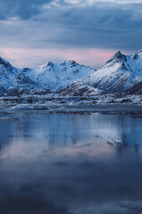 Fototapeta premium Cloudy sundown sky over snowy mountains located on shore of frozen sea