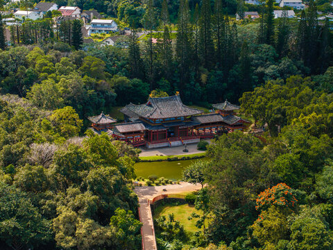 The Byodo In Temple in Oahu, Hawaii, features intricate architecture with red accents, set amidst a manicured garden, pond, and tall trees.
