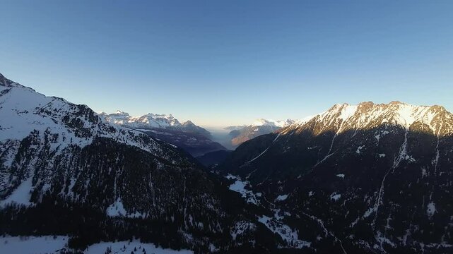 Snow-covered ski slopes and alpine forests frame the serene Champex Lac, Switzerland, as the sun sets behind the majestic peaks of the Swiss Alps in winter.