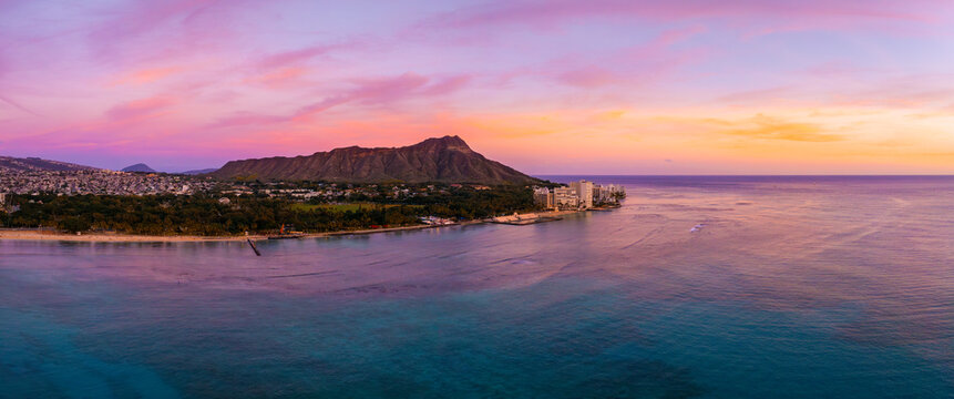 Aerial view of Waikiki Beach in Honolulu, Oahu, Hawaii, at sunset with Diamond Head Crater in the background and vibrant skies over turquoise waters.