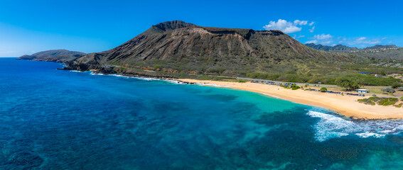 Obraz premium Aerial view of Oahu Island's beach with turquoise waters, golden sand, and Diamond Head crater in the background under clear blue skies.