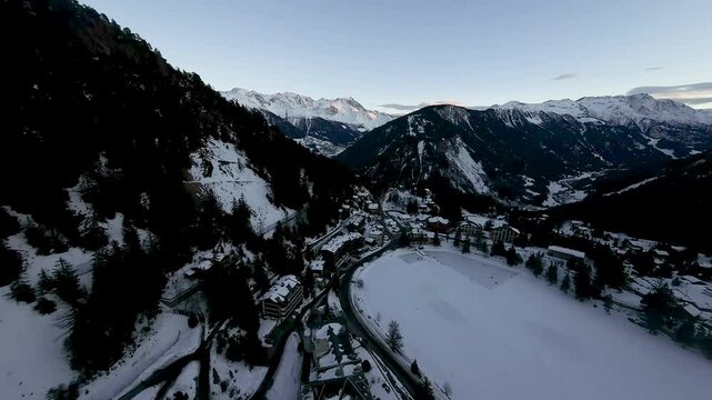 The peaceful winter landscape of Champex Lac in the Swiss Alps, with snow-covered trees, frozen lake, and alpine ski resort, bathed in the soft light of dusk.