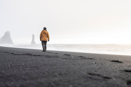 Anonymous solitary figure walking on Reynisfjara Beach in winter