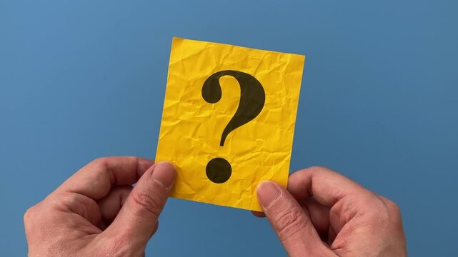 A man holding a yellow paper note with a Question mark on it in his hands over a blue background.