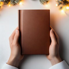 A pair of hands holding a beautiful brown leather book against a softly lit holiday backdrop,...