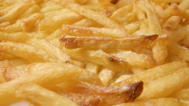 Close-up of sprinkling salt on French fries with a sliding motion.