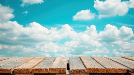 A close-up of wooden planks stacked against a bright blue sky with fluffy white clouds, highlighting the natural texture and warm tones of the wood.