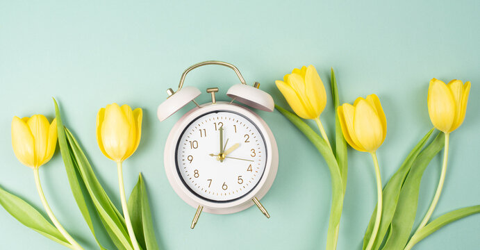 Alarm clock with yellow tulip flowers, switch to daylight saving time in spring, summer time changeover