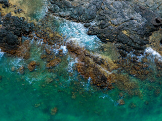 Rugged volcanic rocks meet turquoise Pacific waters on Oahu's coastline. Waves crash, creating...