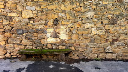 A moss-covered wooden bench sits quietly against an aged stone wall, evoking a sense of history and...