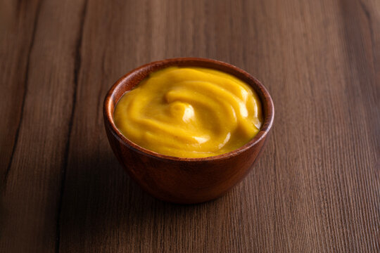 Mustard yellow sauce bowl on wooden background