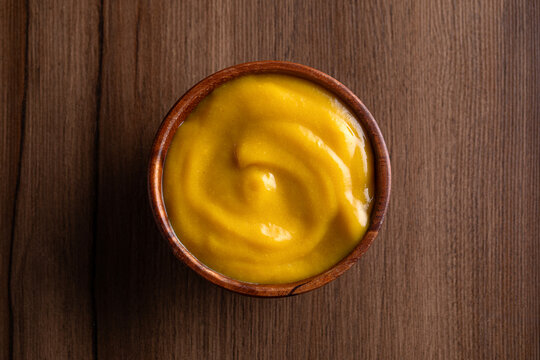 Mustard yellow sauce bowl on wooden background