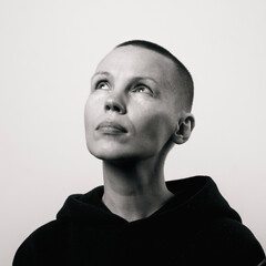 Contemplative caucasian female adult with shaved head in black hoodie