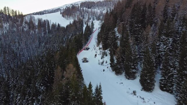 Two snowcats preparing ski slopes. Aerial view of the two vehicles between trees in the mountains in winter