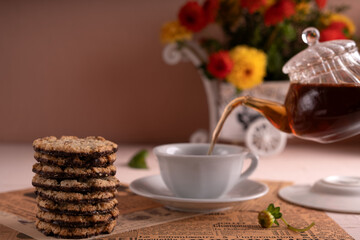 photo Delicious Stack of Chocolate Cookies and Freshly Brewed Tea in Elegant Setup with Cozy Flowers and Vintage Newspaper Ambience in Serenity