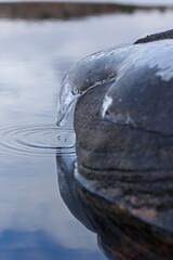 Ice covered rock on waters edge, with frozen water drops.