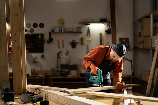 Female carpenter using a jigsaw to cut wood in her workshop, demonstrating precision and craftsmanship in woodworking projects.