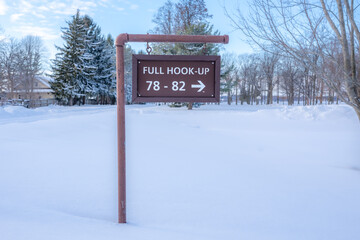Winter, snow covered brown wooden sign Full Hook Up in a park campground.
