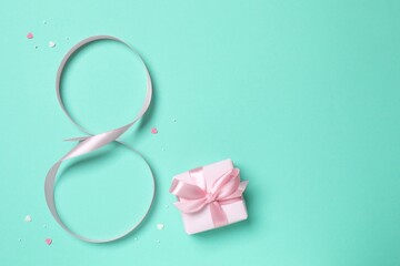 8 March, International Women's Day. Figure eight made of pink ribbon with gift box on a color background. Space for text