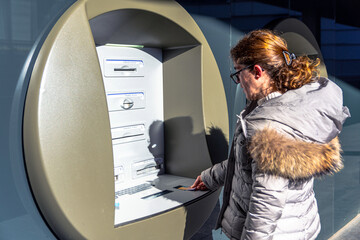 Woman inserting a payment card into an outdoor ATM on a sunny day