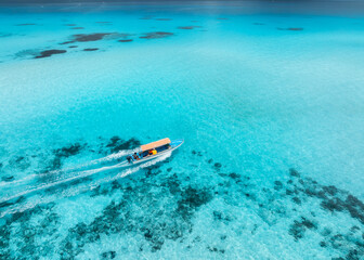 Aerial view of floating boat in clear turquoise water in summer. Zanzibar island. Top drone view of yacht, sandbank in low tide, transparent blue sea, white sand. Background for vacation, travel