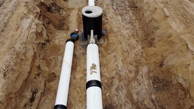 Two gleaming white conduits of engineering infrastructure buried beneath the surface. The site of a project involving the installation of gas, water, and oil pipelines. A close-up view of the camera.