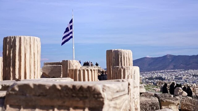 Tourist visitors on ancient Acropolis greek ruins, greek flag, historic landmark in Greece. Summer tourism destination in Europe.