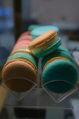 Close-up of colorful macarons with white cream filling displayed under soft lighting on a countertop with a blurred background and selective focus highlighting their delicate texture and vibrant hues