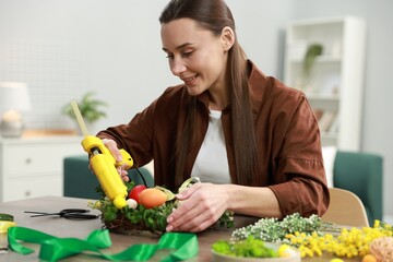 Woman with hot glue gun making craft at table indoors