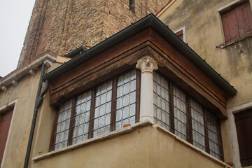 Glass corner window in a Venetian old house next to a tower on a small narrow street in Venice, Italy