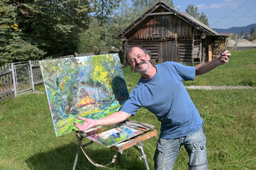 Cheerful artist poses next to his newly painted painting.