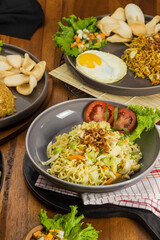 Enjoy a variety of flavorful dishes including noodles with vegetables, fried egg, and snacks served on wooden table for a delightful meal