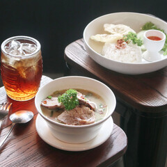 A bowl of flavorful soup with tender meat sits alongside a plate of rice and iced tea, creating a delightful dining experience