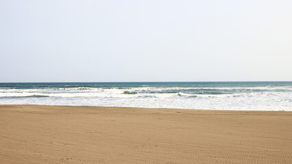 A serene beach features soft sand and rolling waves under a bright blue sky, inviting relaxation and enjoyment of nature