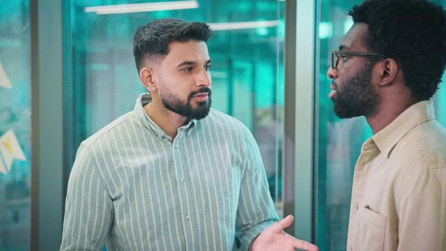 Two handsome men talking with each other. Discussing possible improvements for company. Thinking about solution for difficult task. Office with glass walls. Wearing official clothing.