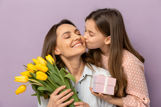 mom and daughter A joyful mother receives a kiss from her daughter while holding yellow tulips and a gift, set against a soft purple background.