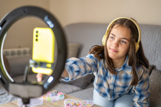 Girl wearing headphones is recording a video blog about colorful bracelets using her smartphone and a ring light, creating engaging content for her online audience