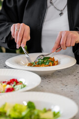 A person elegantly dining, using a fork and knife to enjoy a deliciously presented dish garnished with fresh herbs. Tasteful plating enhances the dining experience on a stylish table.